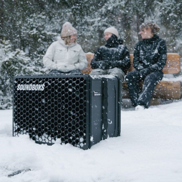 3 Personen im Schnee hören Musik aus einem Lautsprecher