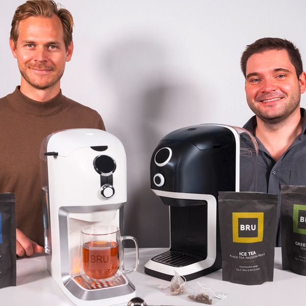 The two BRU founders stand in front of a white and a black tea machine