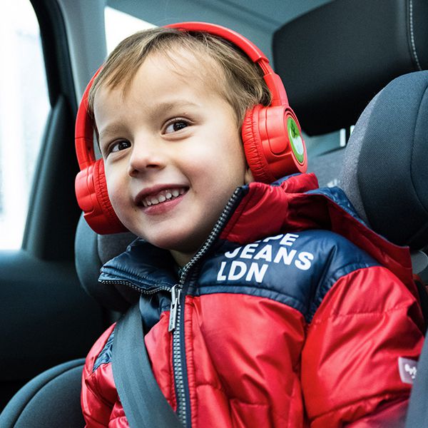Lachendes Kind sitzt im Auto und hört Hörbücher aus einem roten Kekz Kopfhörer